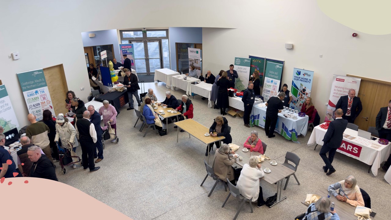 A view of a community hall with displays and people meeting at tables.